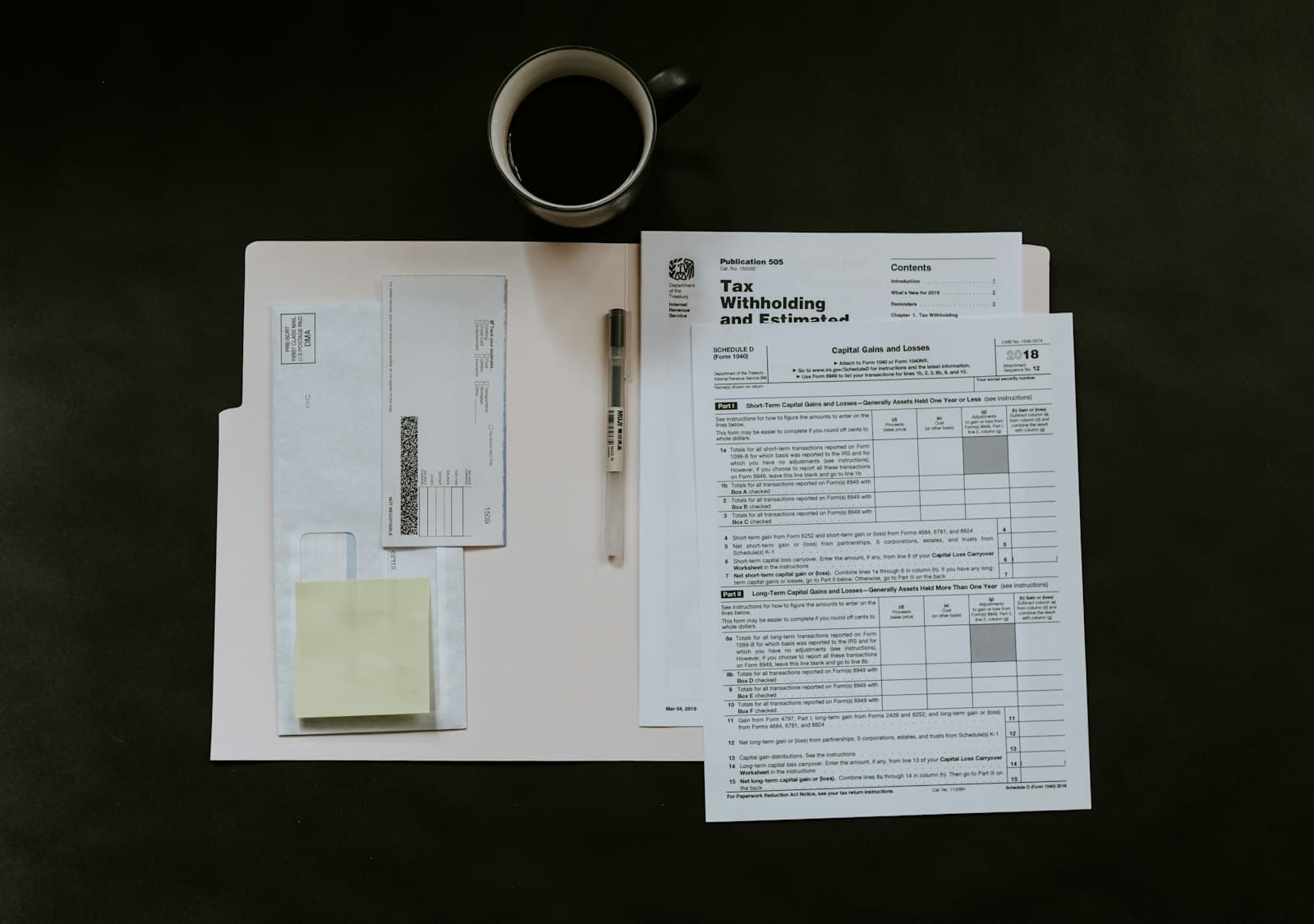 Tax forms, a pen and coffee on a dark desk